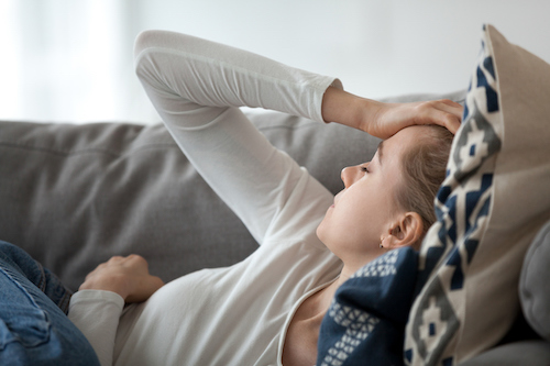 Upset depressed young woman lying on couch feeling strong headache migraine, sad tired drowsy teenager exhausted girl resting trying to sleep after nervous tension and stress, somnolence concept (Upset depressed young woman lying on couch feeling stro