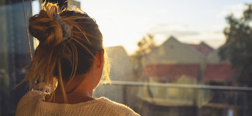 Woman looking through the window at sunset. She is alone and looks a little ad or depressed.